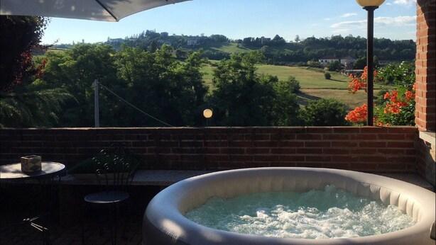 Uma banheira de hidromassagem com vista para uma paisagem verde, uma parede de tijolos e uma mesa com cadeiras.