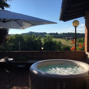 A hot tub with a view of a green landscape, a brick wall, and a table with chairs.