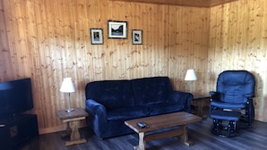 Ein gemütlicher Raum mit einem dunkelblauen Sofa, einem Holztisch, einem schwarzen Liegesessel und einem Fernseher auf einem Schrank.