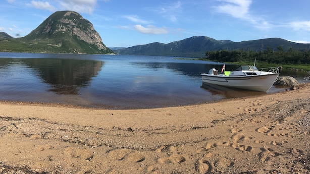 Ein Boot liegt vor einem Sandstrand mit einem Berg im Hintergrund.