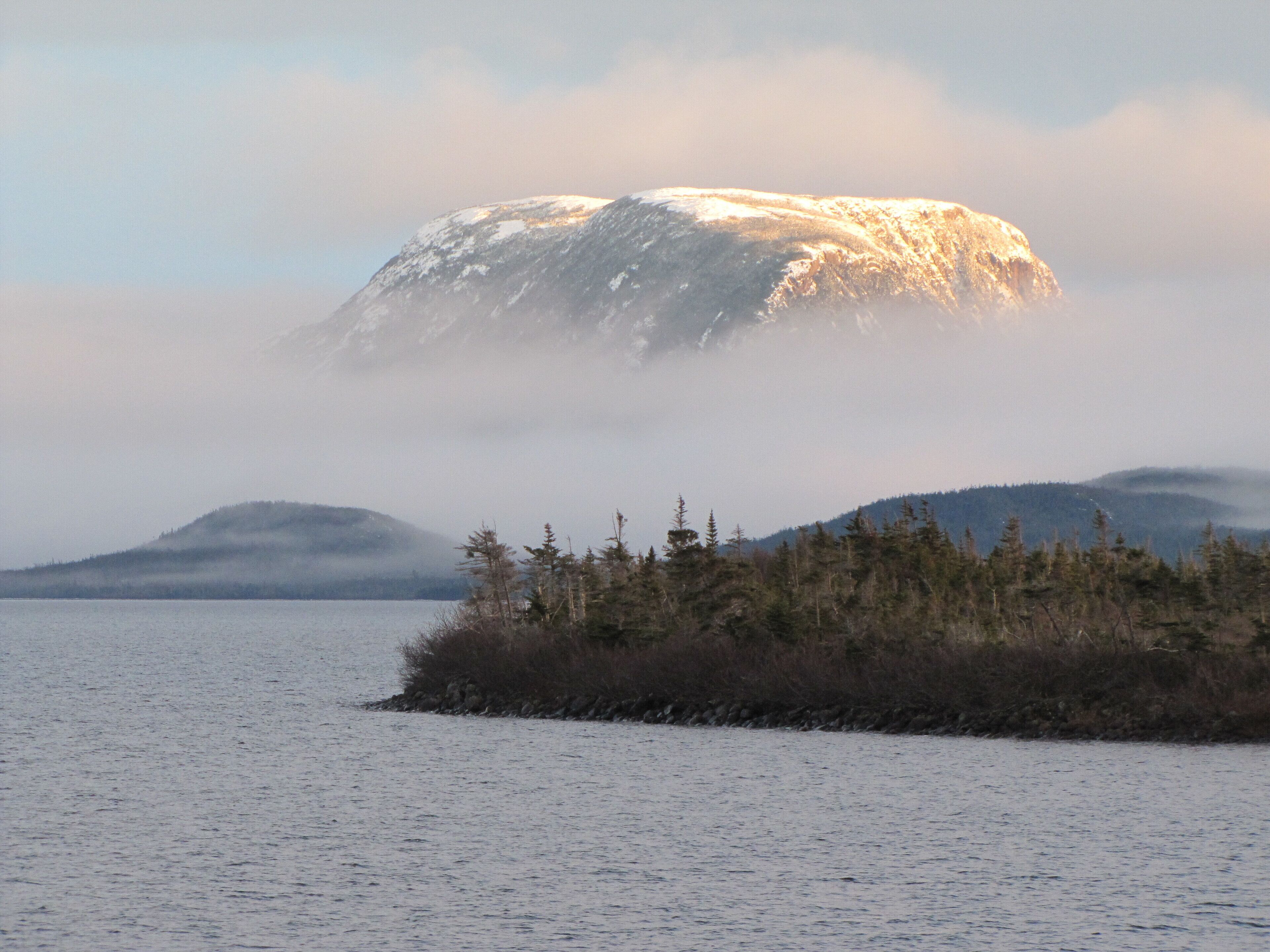 Ein Berg, teilweise von Wolken verdeckt, mit einer bewaldeten Insel im Vordergrund.