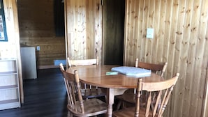 Ein Holzinterieur mit einem runden Tisch, vier Stühlen, einem Kühlschrank und einer Tür zu einem weiteren Raum.