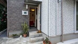 Een modern gebouw met een grijze gevel, een kleine inkom met treden en plantenbakken.