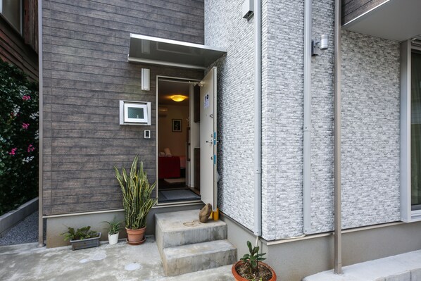 A modern building with a grey exterior, a small entrance with steps, and potted plants.