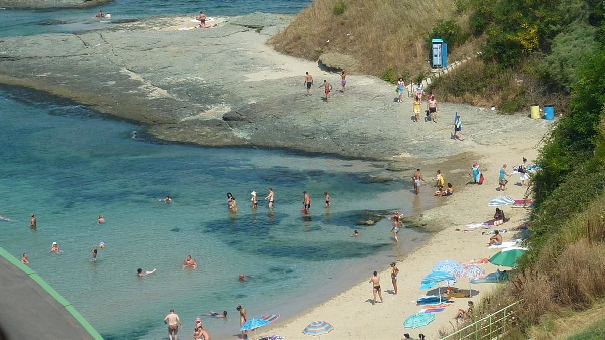 Una playa con agua cristalina, gente nadando y tomando el sol, y sombrillas en la arena.