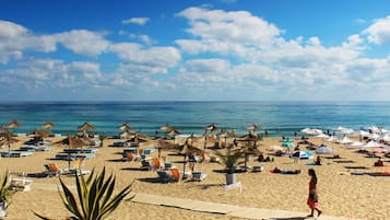 Una playa con filas de tumbonas y sombrillas, un cielo azul despejado y el océano al fondo.