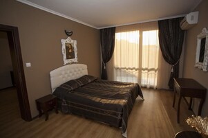 Un dormitorio con una cama grande, una mesita de noche, un armario pequeño, un espejo y una ventana con cortinas.