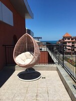 Un balcón con una silla de mimbre y vista al mar.