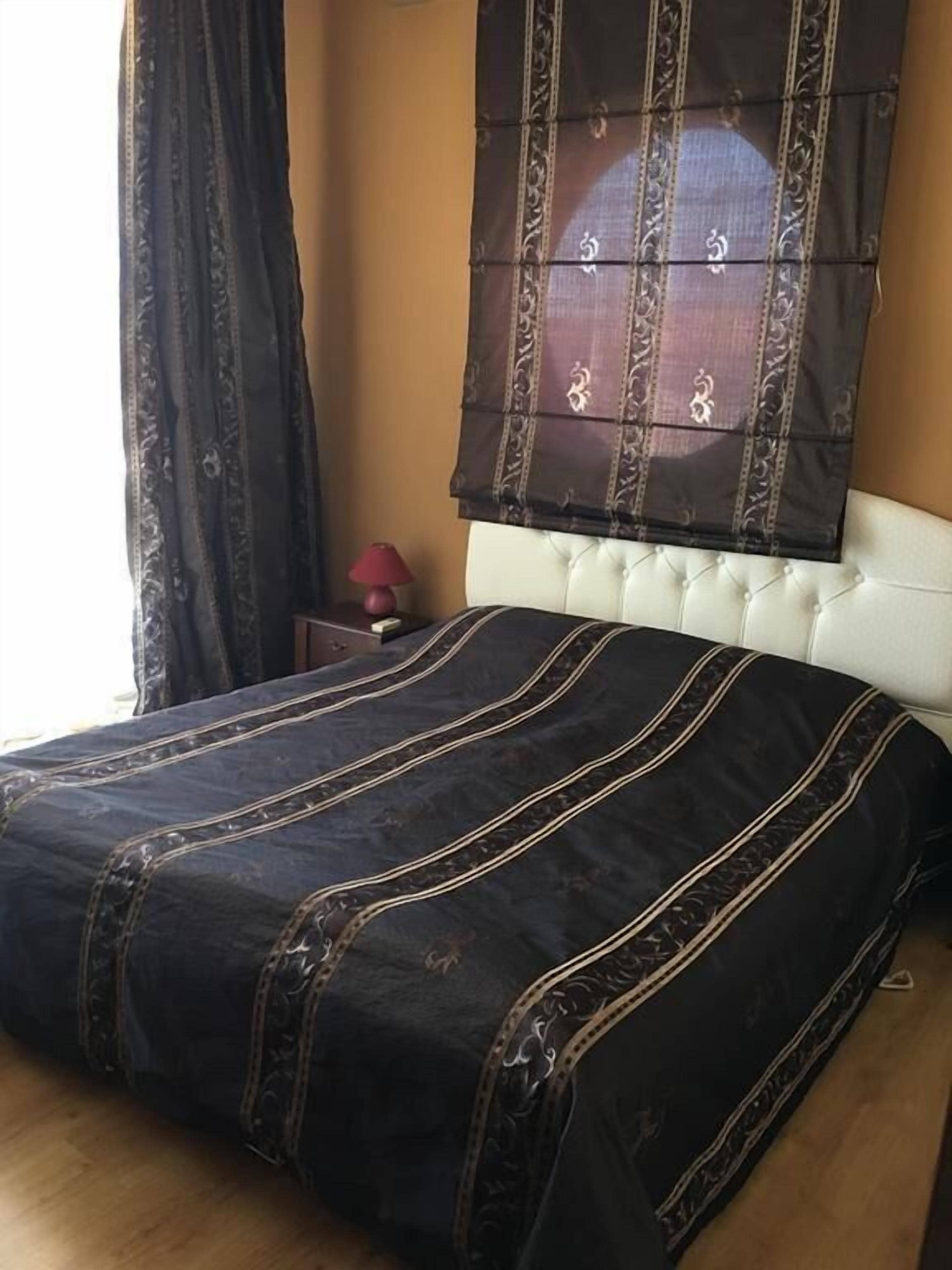 A bedroom with a bed, a nightstand, a lamp, and a window with curtains.