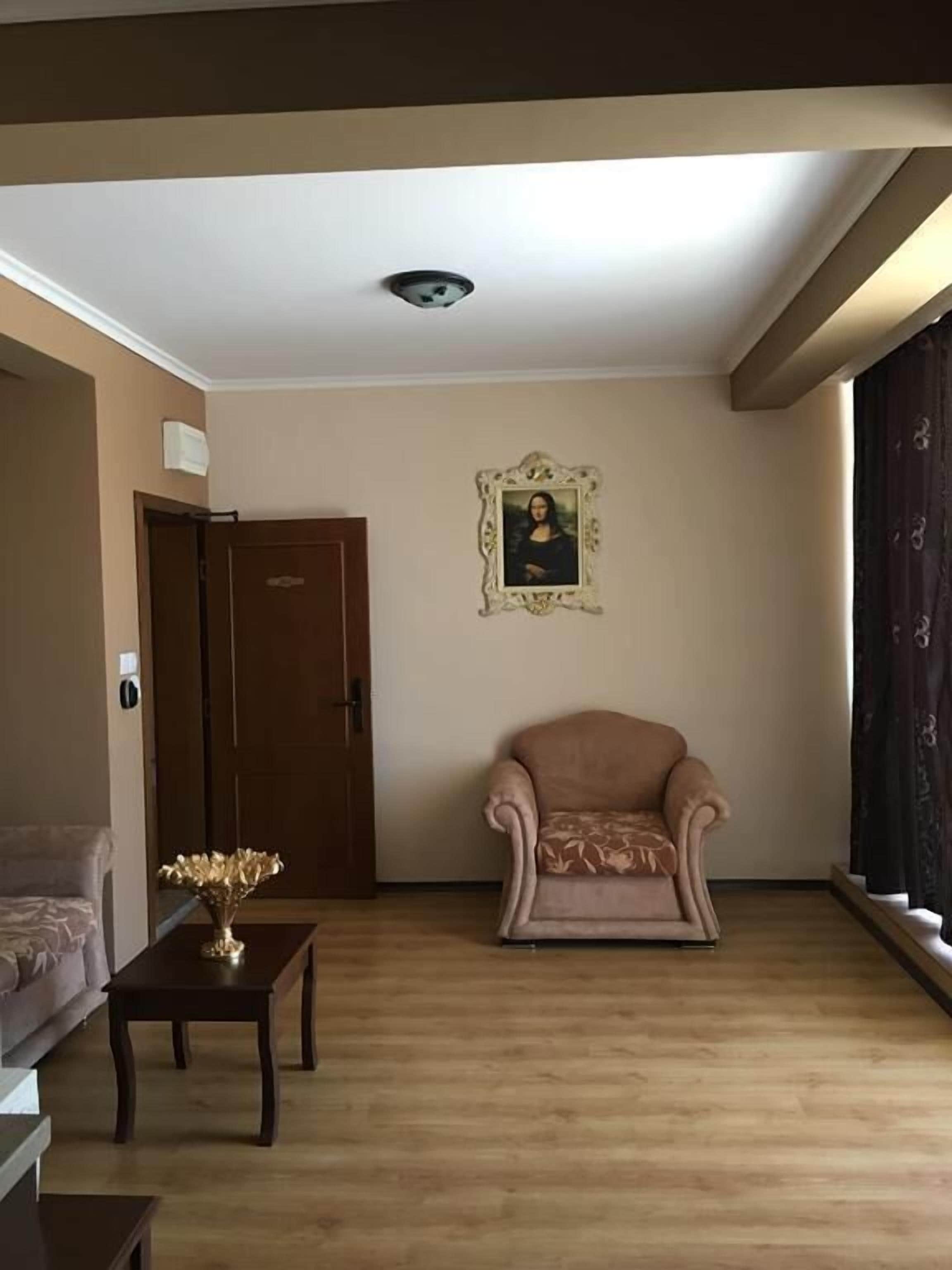 Una sala de estar con un sofá beige, una mesa de centro de madera con un jarrón decorativo, un cuadro en la pared y una puerta al fondo.