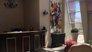 A reception area with a dark reception desk, a chandelier, a large colorful painting, and a potted plant. - Red Hotel - Lozenetz (Tsarevo)