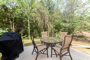 Relax outdoors with a round table and comfortable seating for four, surrounded by lush trees and a wooden deck.