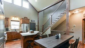 Een ruime keuken met houten kasten, een groot eiland en een eethoek met een houten tafel en stoelen.