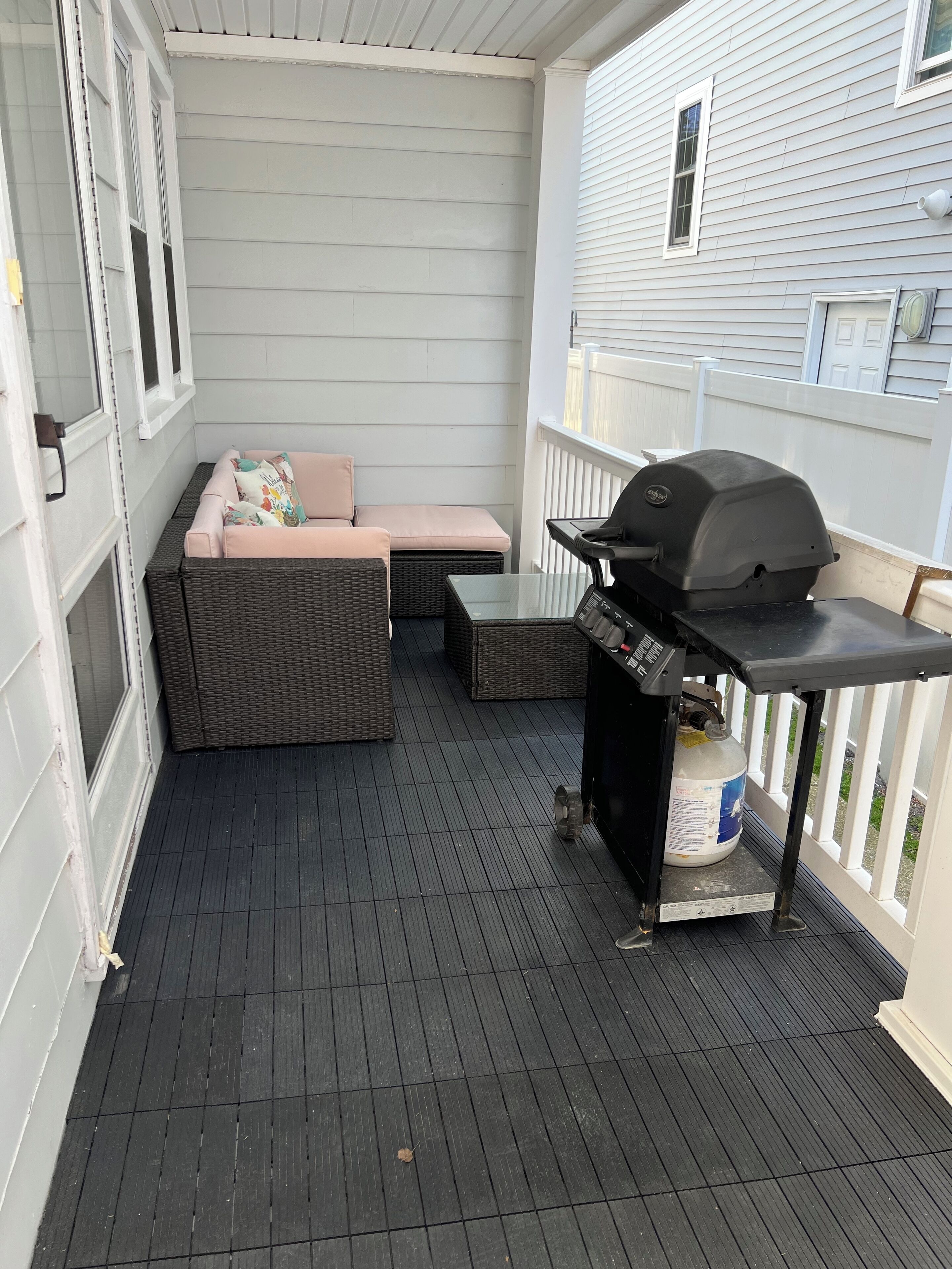 Un patio techado con una parrilla, muebles de mimbre y una zona de estar acolchada.