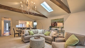 Een ruime woonkamer met een hoge plafond, een kroonluchter, een ronde salontafel en een grote hoekbank.