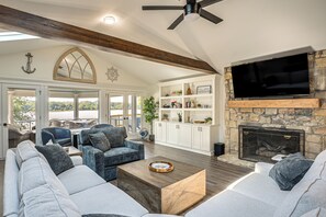 A spacious living room with a stone fireplace, a large flat-screen TV mounted on a stone wall, and a cozy seating area with a sofa and armchairs.