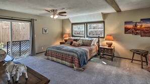 A bedroom with a large bed, a ceiling fan, a window with a view, a nightstand, and a small table. - Charming Texas Home w/ Stunning Canyon Views! (Canyon)