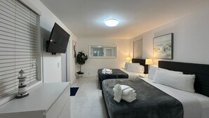 Una habitación de hotel con dos camas, un televisor de pantalla plana, una planta en maceta y un cuadro en la pared.