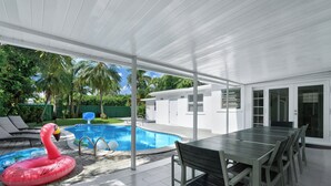 Un espacio al aire libre techado con piscina, mesa de comedor y sillas.