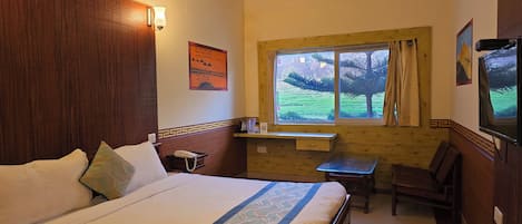Habitación de hotel con cama, escritorio, silla, ventana con vistas a zonas verdes y televisión instalada en la pared.