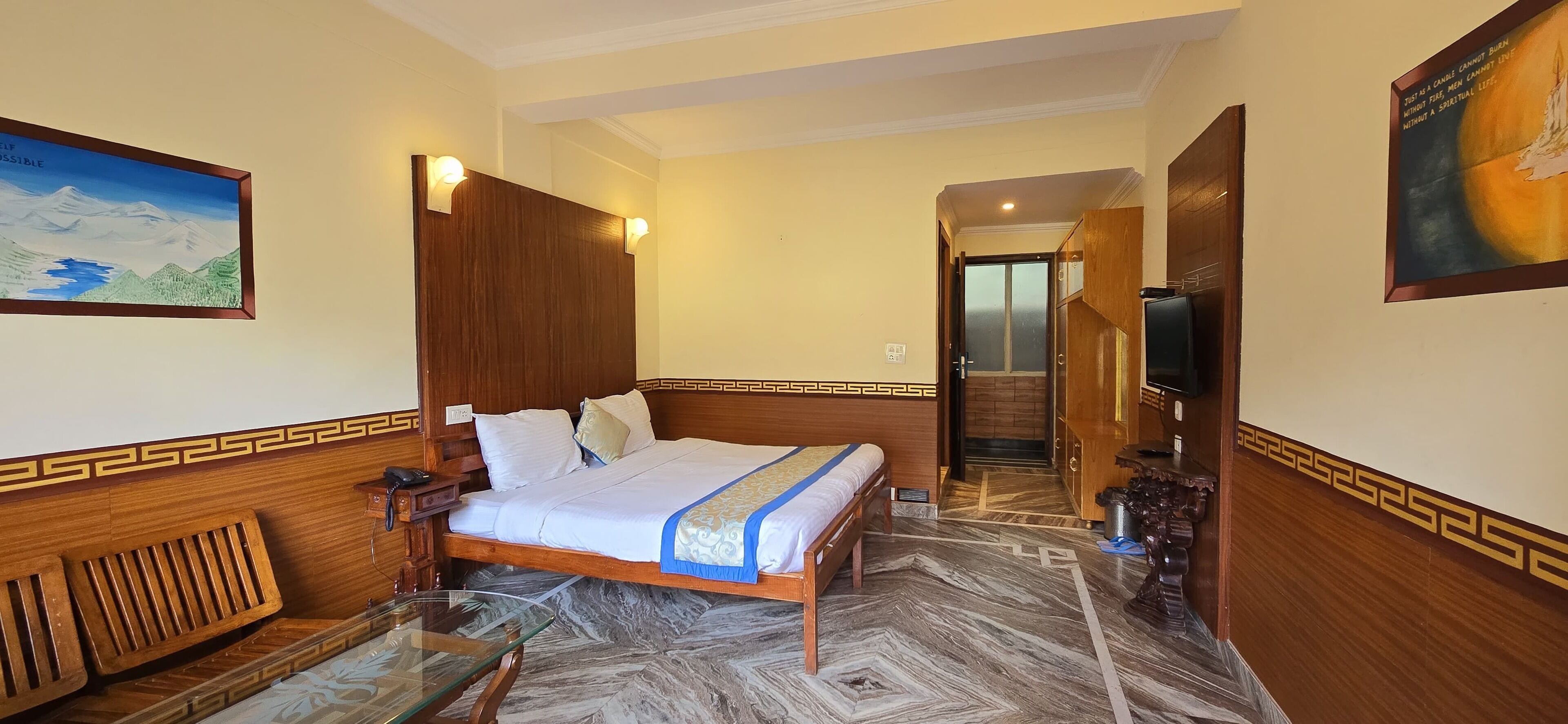 Una camera d'albergo con un letto di legno, un tavolino in vetro, un quadro appeso alla parete e vista sul corridoio.