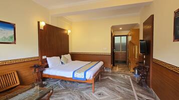 Una camera d'albergo con un letto di legno, un tavolino in vetro, un quadro appeso alla parete e vista sul corridoio.