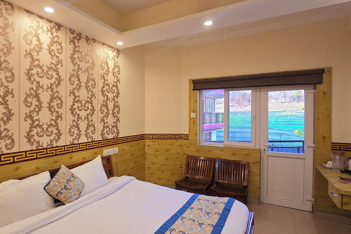 Habitación de hotel con una cama grande, cabecero de madera, papel tapiz estampado, una ventana con vistas y una mesita con hervidor.