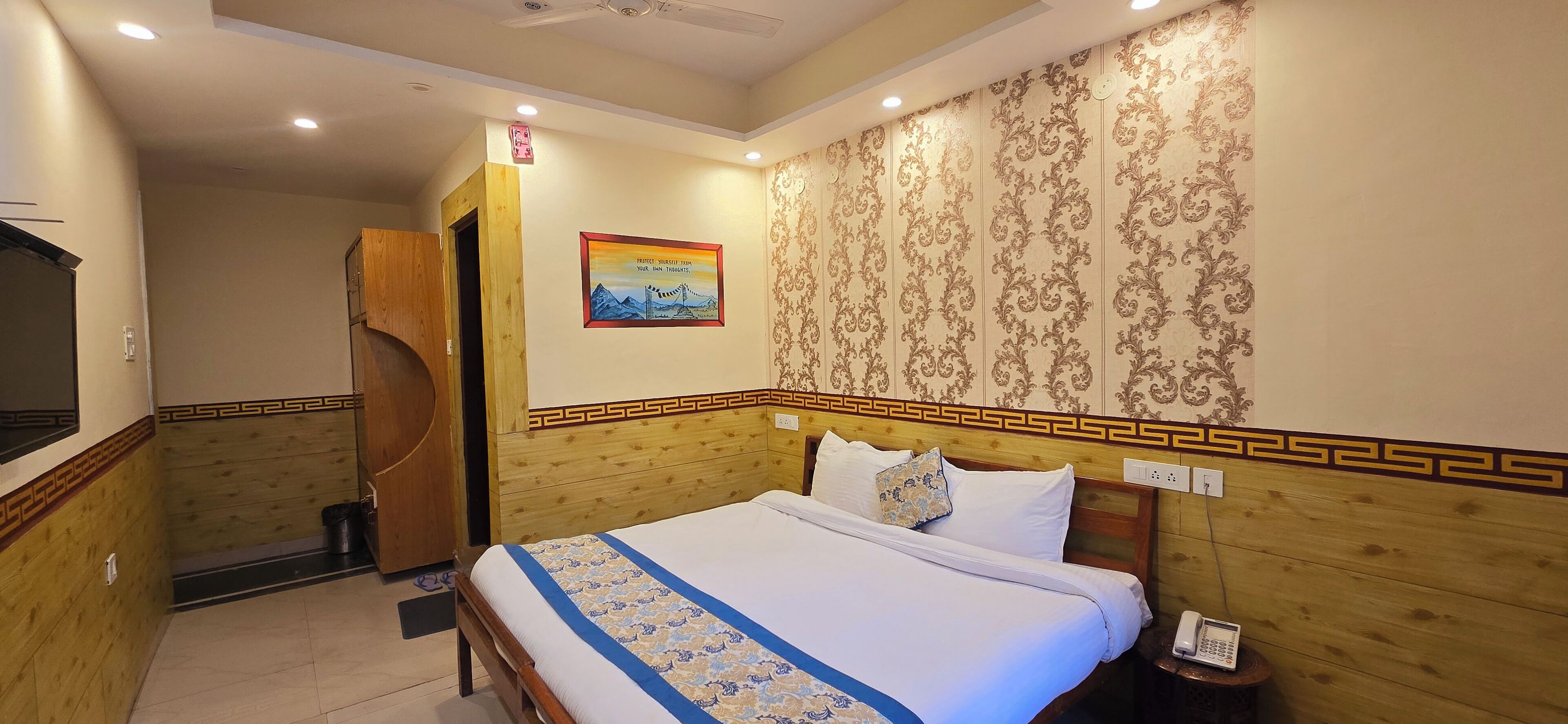 A hotel room with a wooden headboard, a bed with a patterned bedspread, a nightstand with a phone, and a painting on the wall.