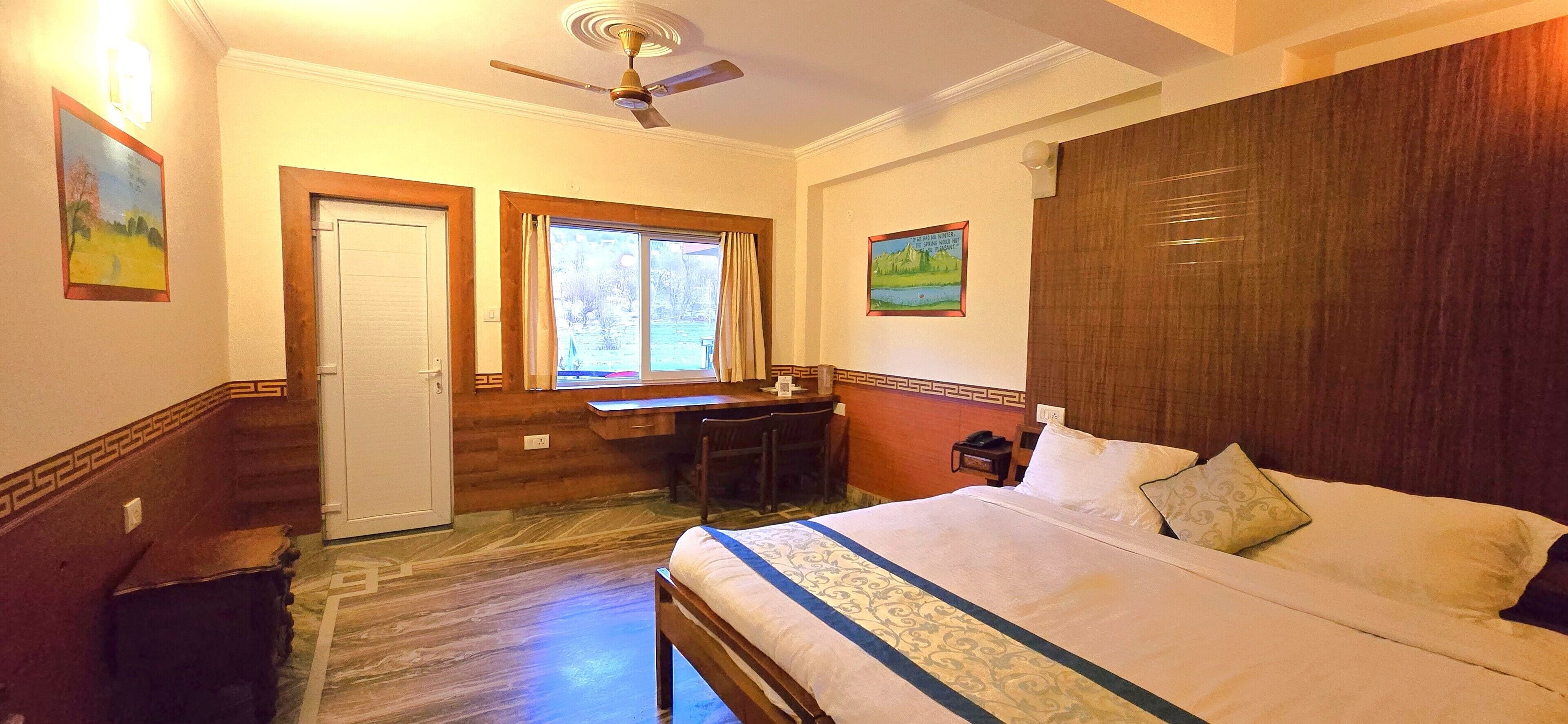 A hotel room with a bed, desk, and window.