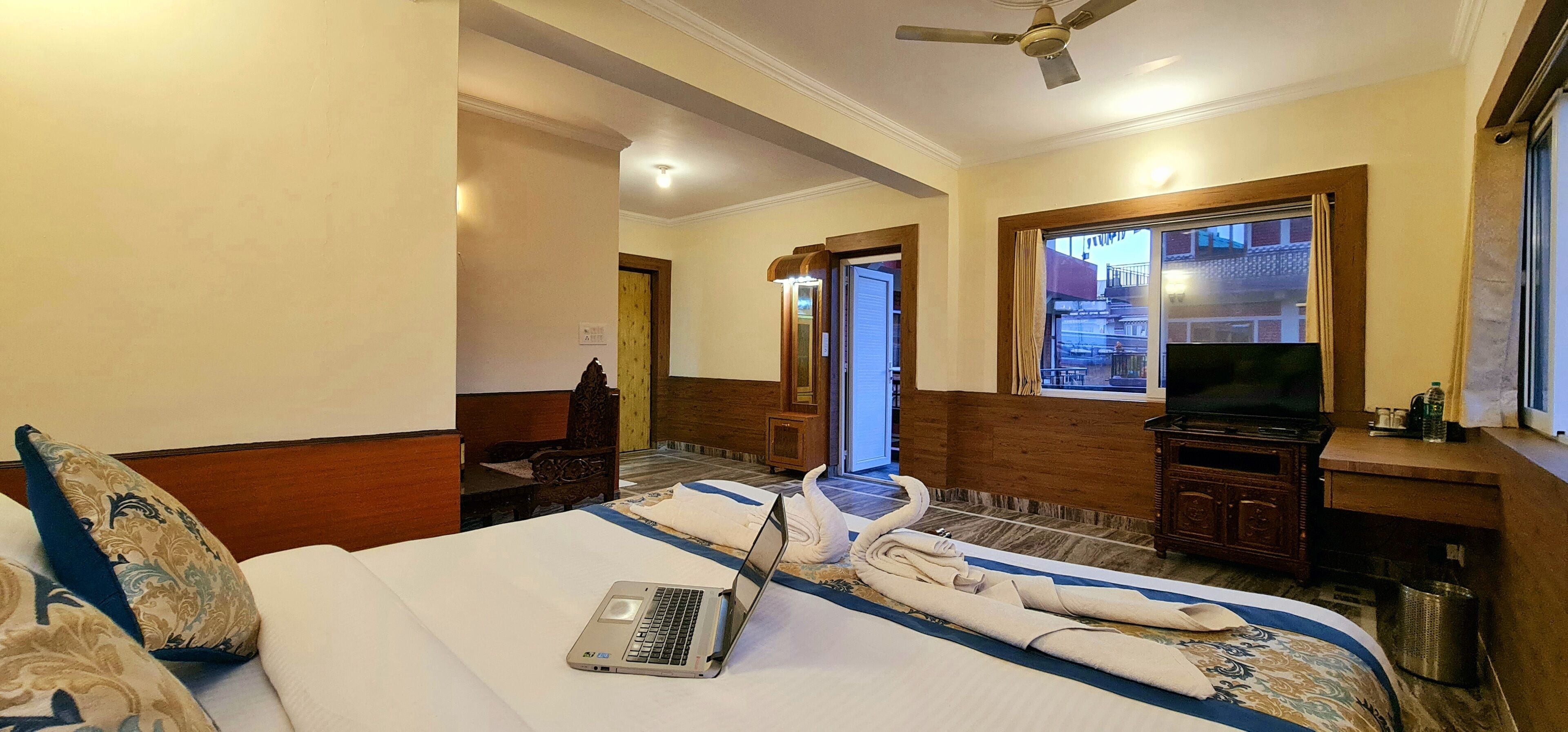 A hotel room with a bed, a laptop, a TV, and a view of the outside.