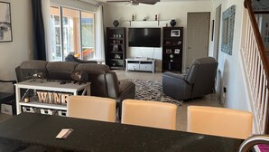 Ein Wohnzimmer mit Sofa, Sesseln, einem Couchtisch, einem Fernseher und einem Bücherregal.