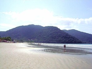 A beach with a mountain in the background and a few people walking along the shore.