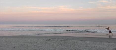 A beach scene with a person fishing.