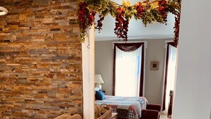 A bathroom with a stone wall, a wooden vanity, a mirror, and a bed visible through an archway. - Centennial Inn Bed & Breakfast (Conneaut)