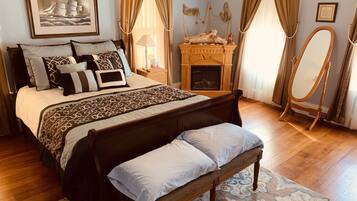 Une chambre à coucher avec un grand lit, un banc en bois, une commode, un miroir et une cheminée.