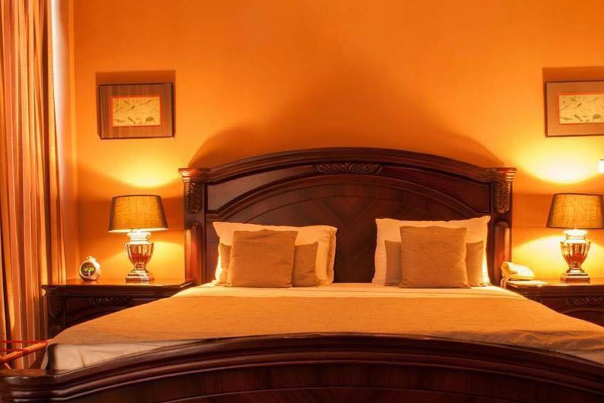 Quarto de hotel com uma cama grande, duas mesas de cabeceira com luminárias e quadros nas paredes.