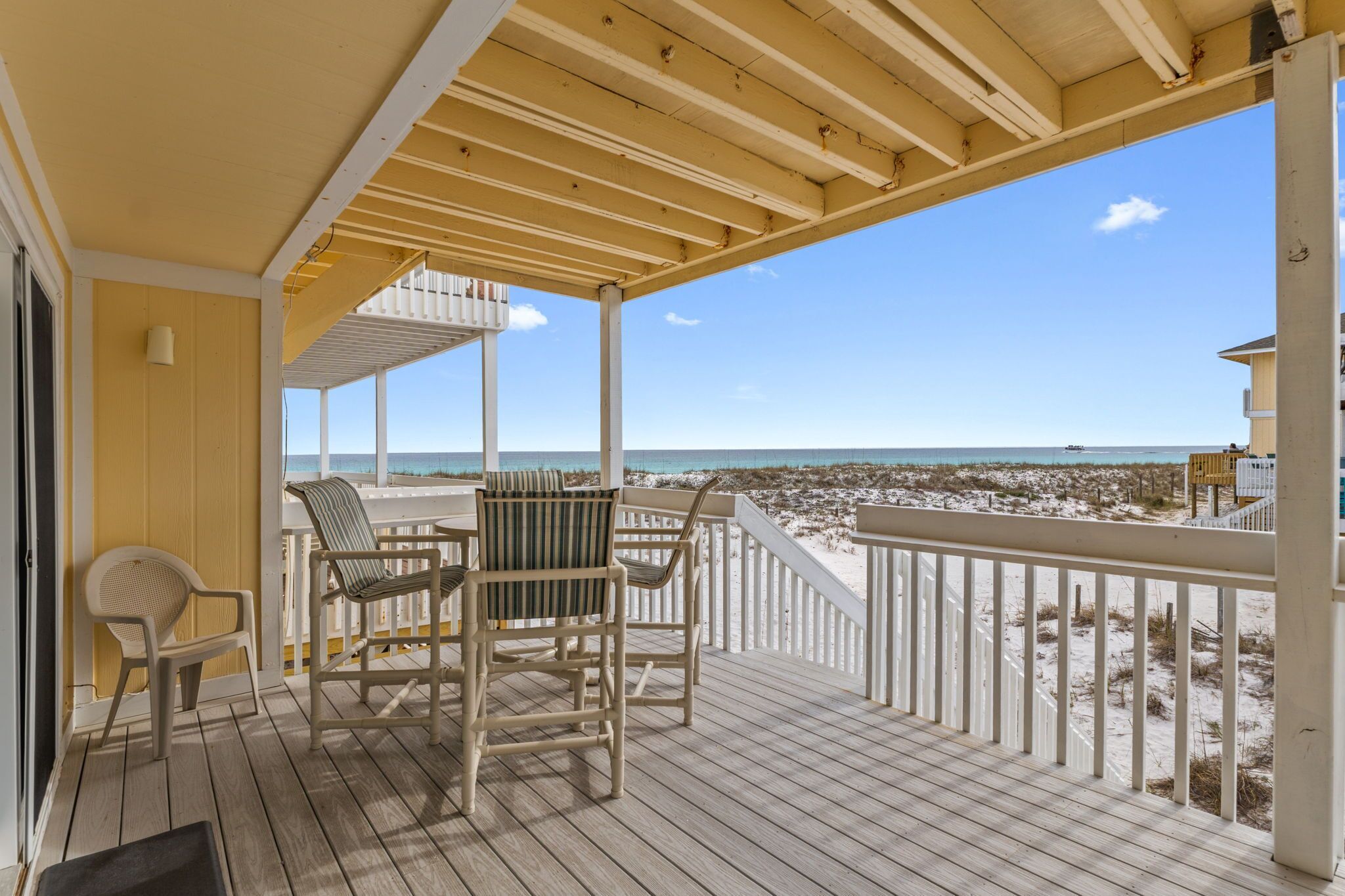 A covered deck with a view of the beach, featuring a table and two chairs.