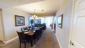 A dining area with a long table, chairs, and a chandelier. There is a large window with a view of the outdoors. - Cozy Oceanfront Retreat, Steps from the Beach | OB 602 (Myrtle Beach)