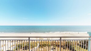 A beach view from a balcony with a railing, sandy beach, and calm sea. - Cozy Oceanfront Retreat, Steps from the Beach | OB 602 (Myrtle Beach)
