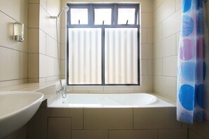 Bathroom features a bathtub, sink, and showerhead, with a large window for natural light.