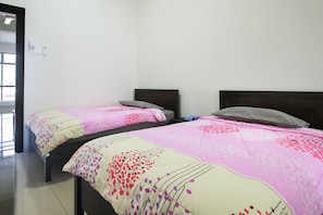 Two single beds with pink and white bedspreads are positioned against a white wall, each with a dark headboard.