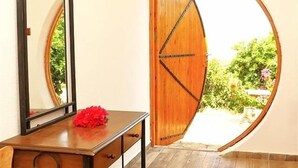 Una habitación con un escritorio de madera, una silla, un espejo y una puerta de madera con un ventanal circular.