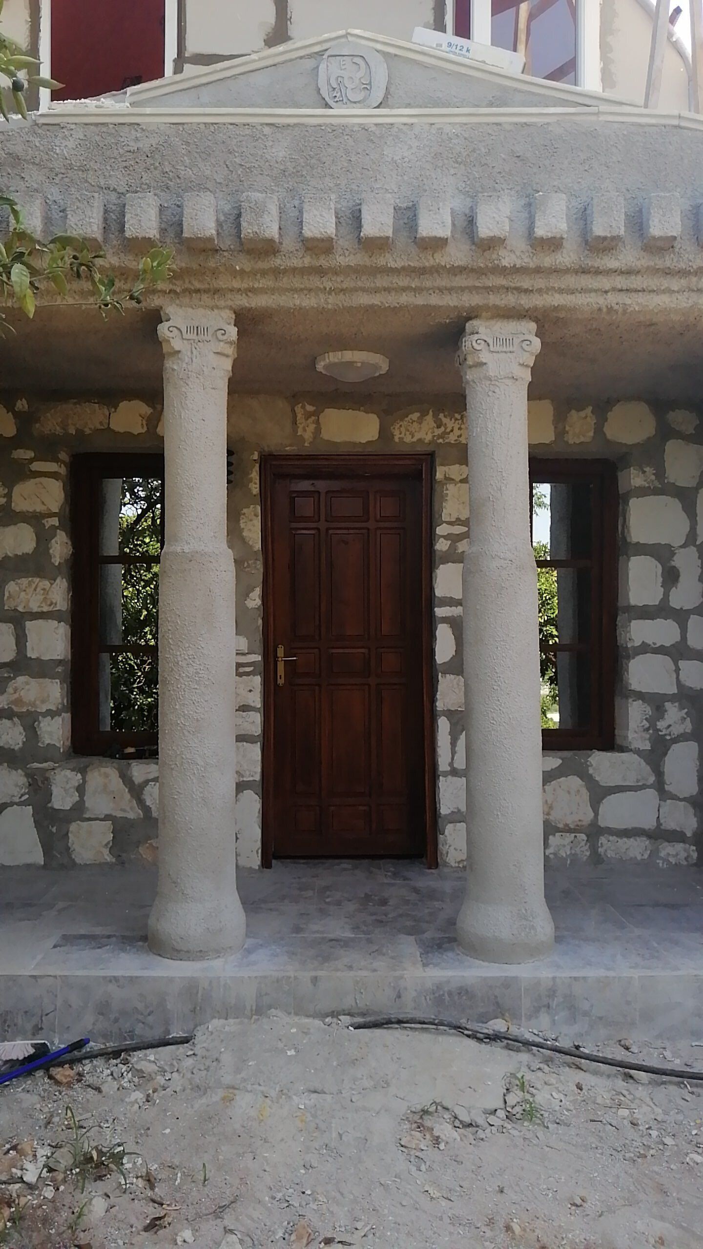 A stone building with a central wooden door, flanked by two columns, and a small overhang above.