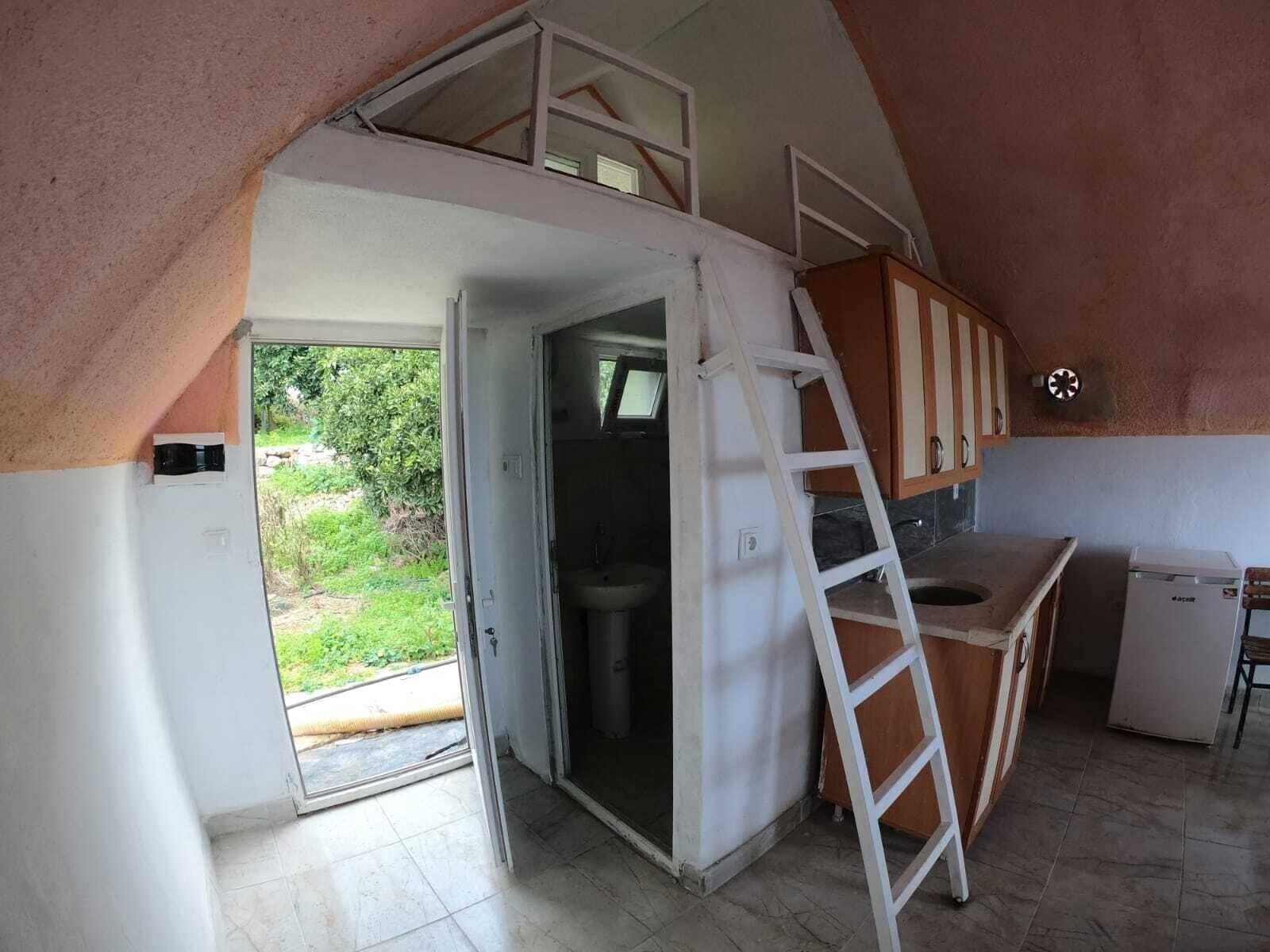 A kitchen with a lofted sleeping area, a ladder, and a small refrigerator.