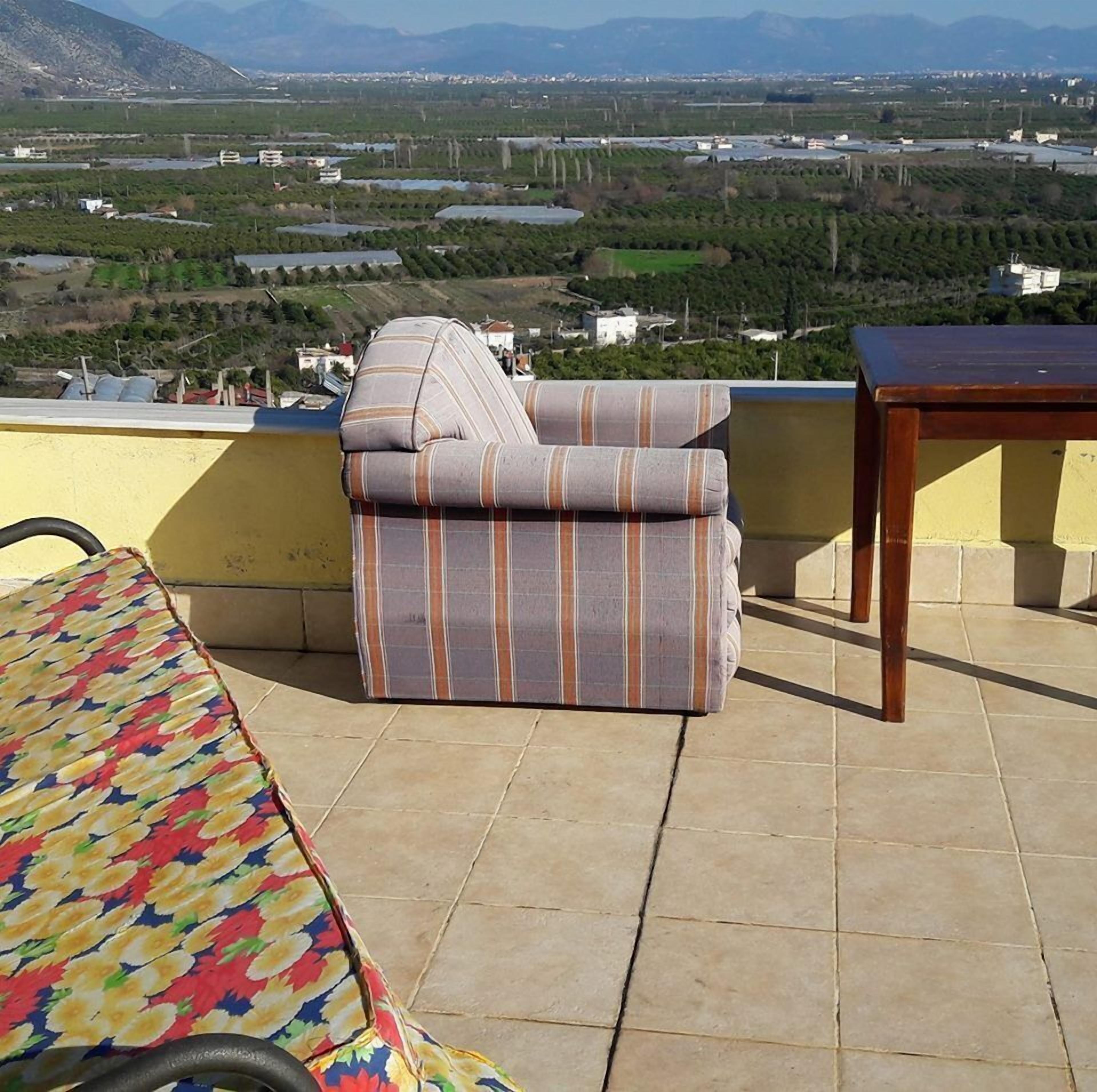 Una terraza con un sofá a rayas y una mesa, con vistas a un paisaje con campos y edificios al fondo.