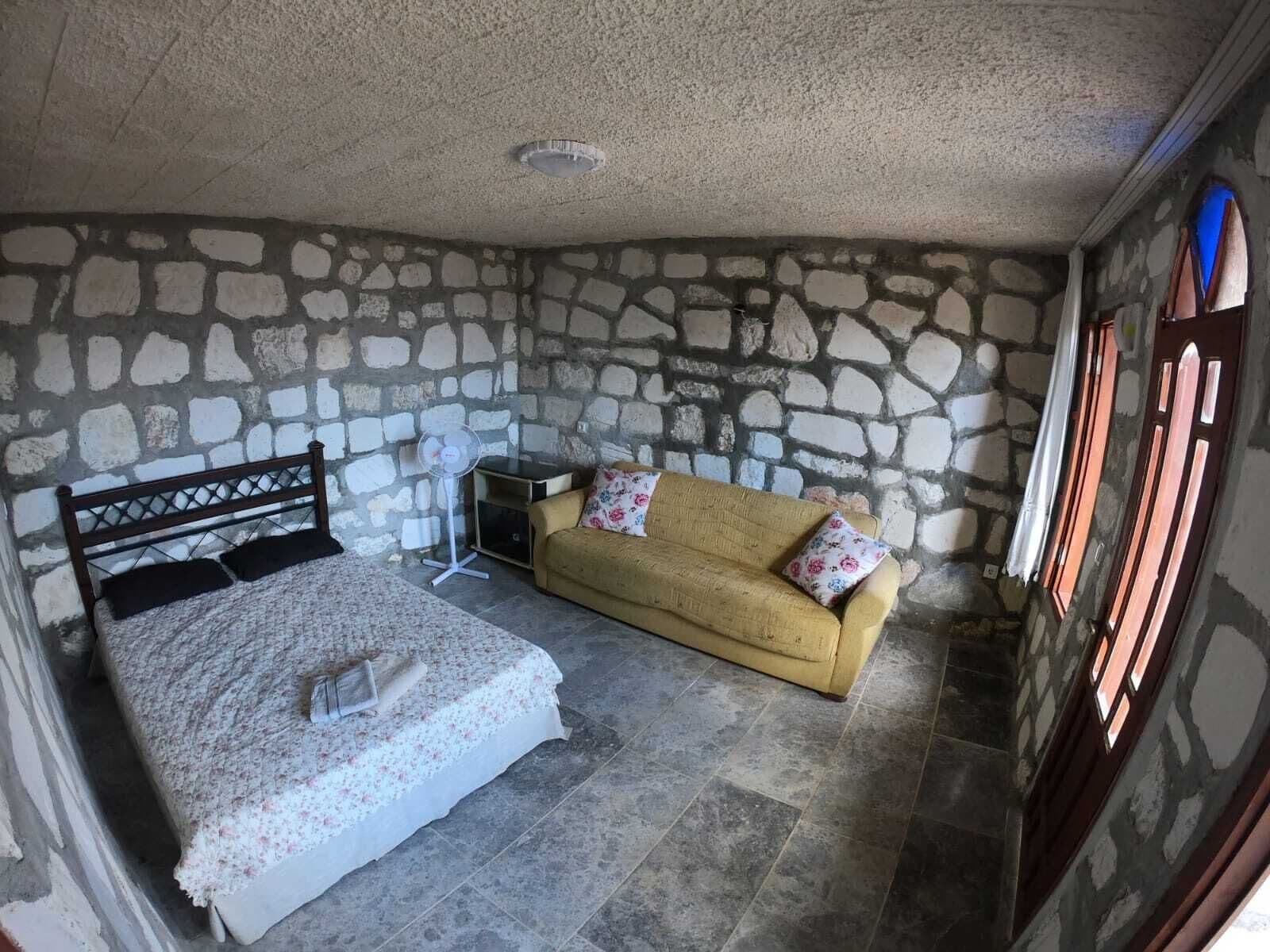 Une pièce avec un mur en pierre, un lit recouvert d’une couvre-lit à motifs floraux, un canapé agrémenté de coussins à motifs floraux et une petite table.