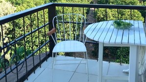 Un balcón con una silla y mesa de metal blanco, con vista a un viñedo.