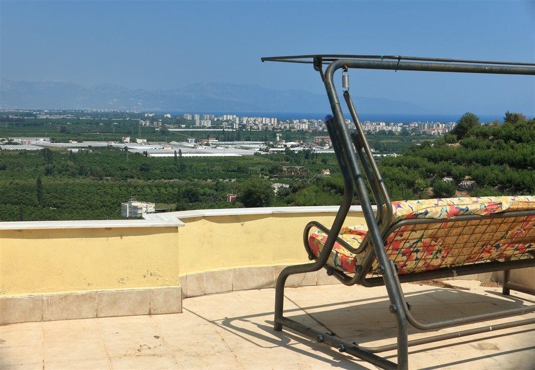 Un banco metálico con un cojín floral en una terraza en la azotea con vistas a un paisaje urbano y montañas.