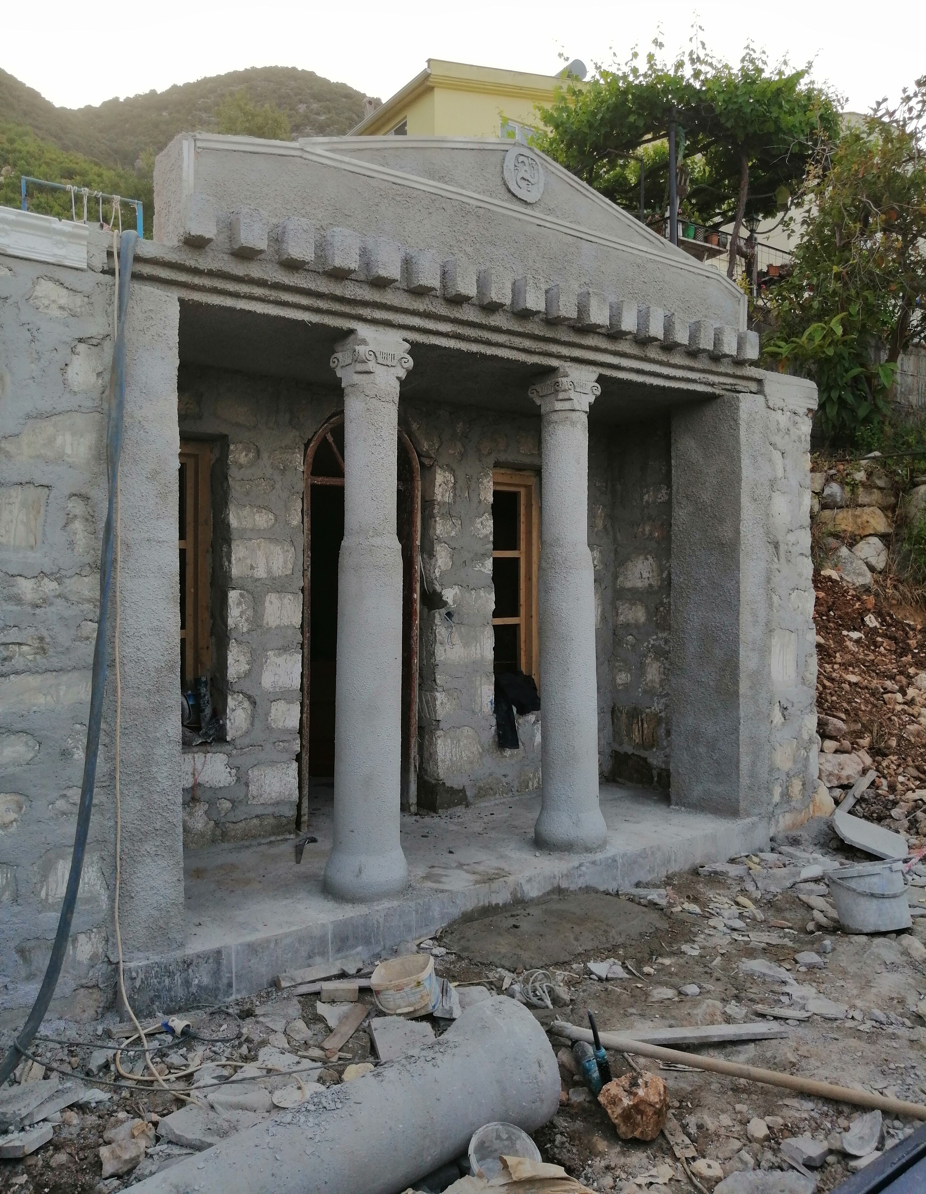 A building under construction with stone columns and a partially open door.