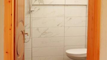 Un baño pequeño con inodoro, ducha y puerta de madera.